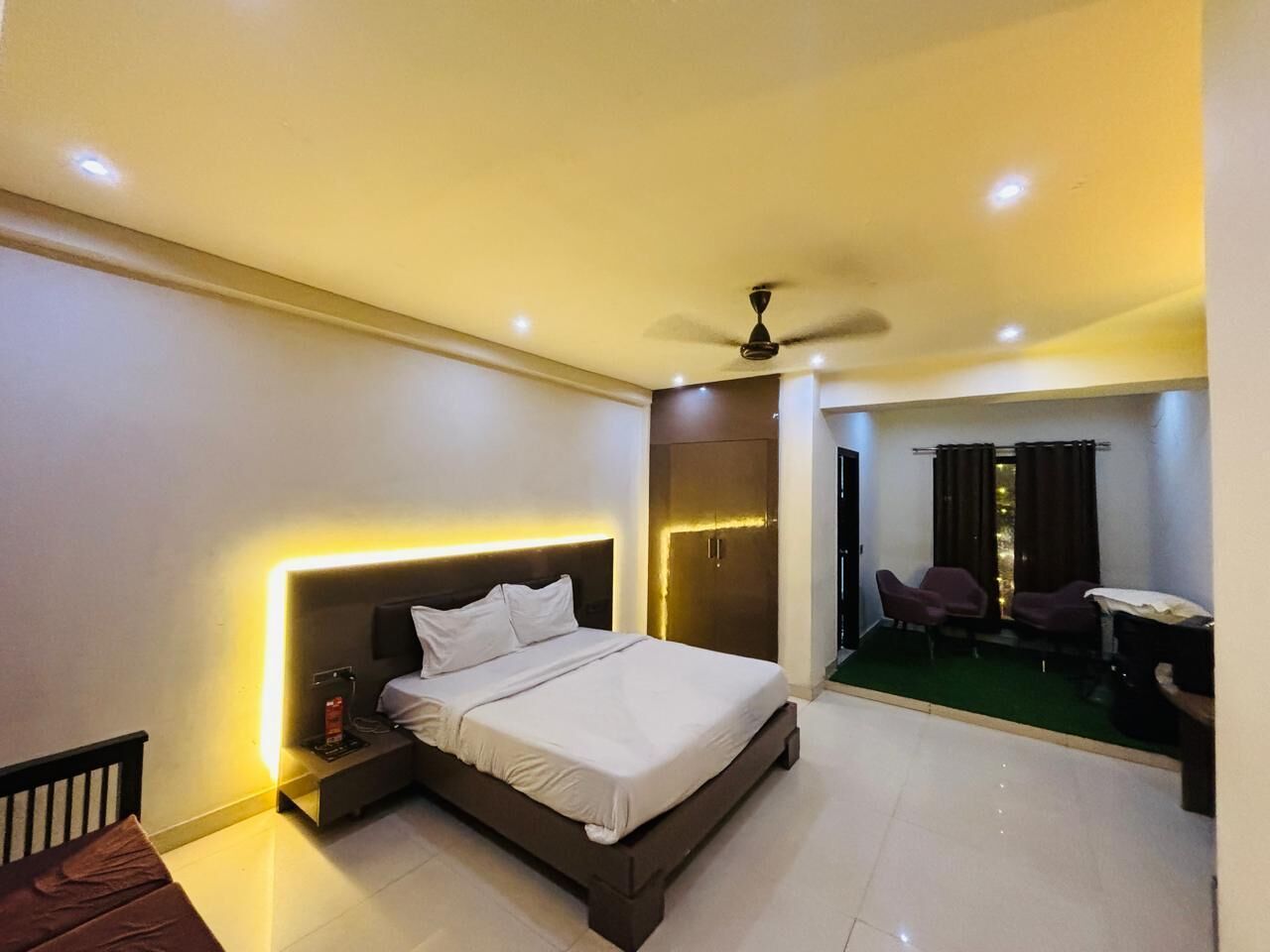 A modern bedroom with a large bed, bedside tables, a ceiling fan, and a small seating area with chairs.