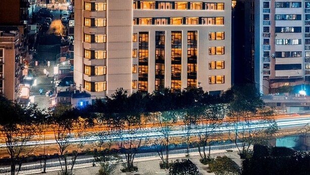 Un hotel con varios pisos, un letrero llamativo y vistas del área urbana al atardecer.