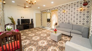 A living room with a grey sofa, a television, a patterned carpet, and a chandelier. - Blue Horizon 2bhk Nr Marina Beach Mylapore (Chennai)