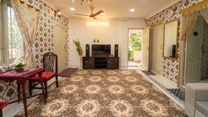A room with patterned wallpaper, a chandelier, a ceiling fan, a television, and a mirror. - Blue Horizon 2bhk Nr Marina Beach Mylapore (Chennai)