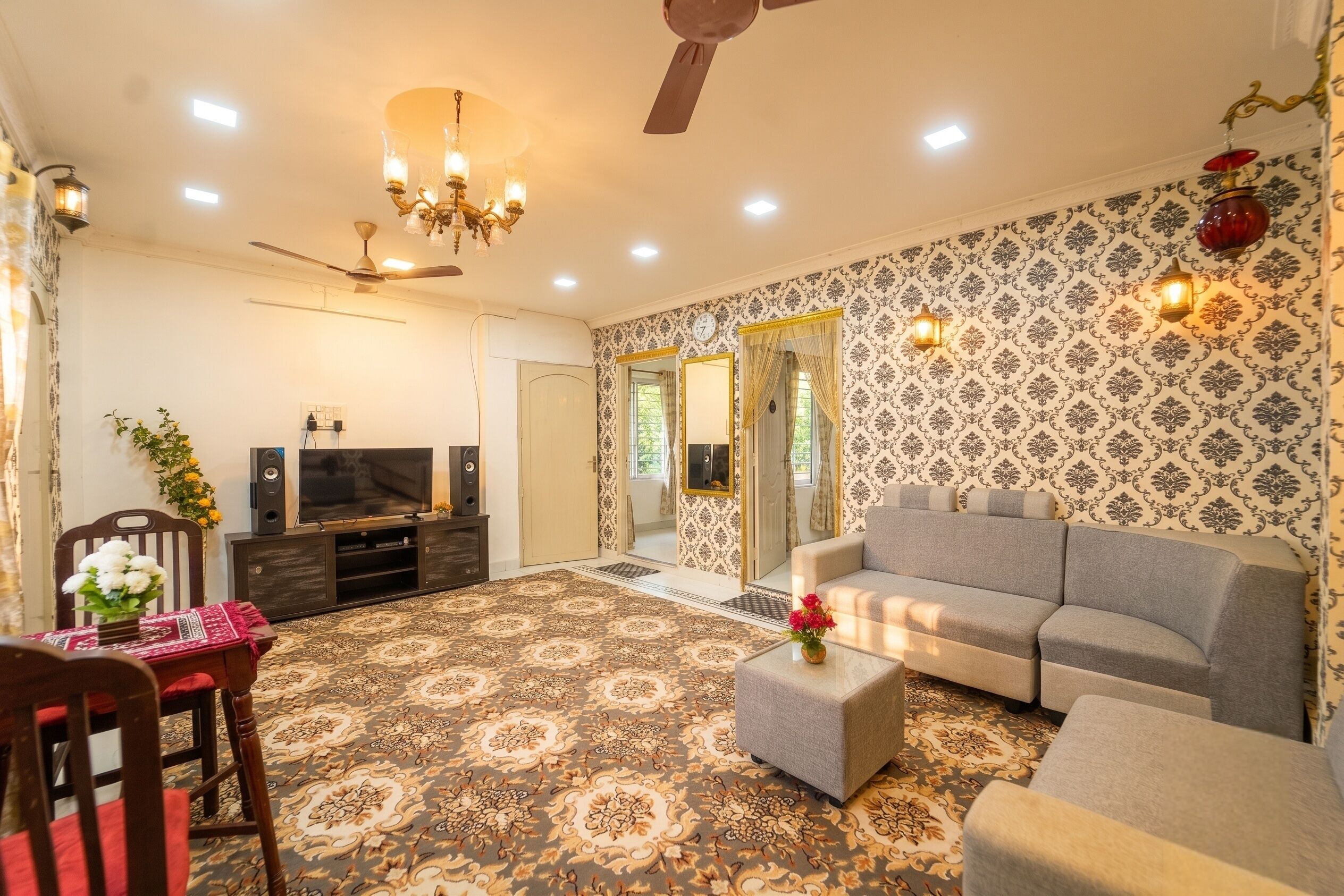 A living room with a sofa, a television, a ceiling fan, and patterned wallpaper.