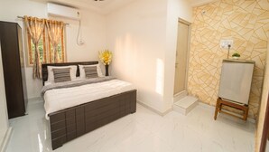A bedroom with a bed, a ceiling fan, an air conditioning unit, a window with curtains, a wall-mounted vase with flowers, and a tiled floor. - Blue Horizon 2bhk Nr Marina Beach Mylapore (Chennai)