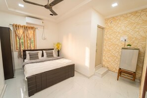 A bedroom with a bed, a ceiling fan, an air conditioning unit, a window with curtains, a wall-mounted vase with flowers, and a tiled floor. - Blue Horizon 2bhk Nr Marina Beach Mylapore (Chennai)