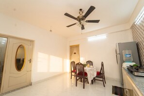 A dining area with a ceiling fan, a table with chairs, a water dispenser, and a refrigerator. - Blue Horizon 2bhk Nr Marina Beach Mylapore (Chennai)