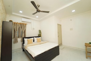 A bedroom with a bed, a ceiling fan, an air conditioning unit, a window with curtains, and a small table with a plant. - Blue Horizon 2bhk Nr Marina Beach Mylapore (Chennai)