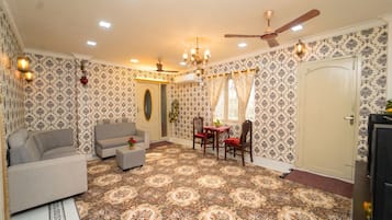 A room with patterned wallpaper, a sofa, a dining table with chairs, a ceiling fan, and a door.