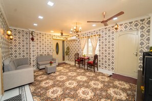 A room with patterned wallpaper, a sofa, a dining table with chairs, a ceiling fan, and a door. - Blue Horizon 2bhk Nr Marina Beach Mylapore (Chennai)