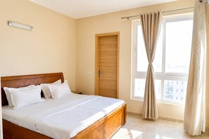 A bedroom with a bed, a wooden headboard, a window with curtains, and a door. - Vrindavan Vista2bhknear Prem Mandiriskcon (Mathura)