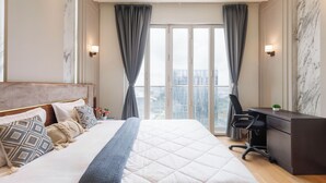 Una habitación de hotel moderna con una cama grande, un escritorio y vistas de la ciudad a través de ventanales de piso a techo.