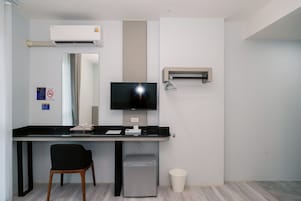 Un espacio de oficina moderno con escritorio, silla, televisor, equipo de aire acondicionado y un cesto de basura.