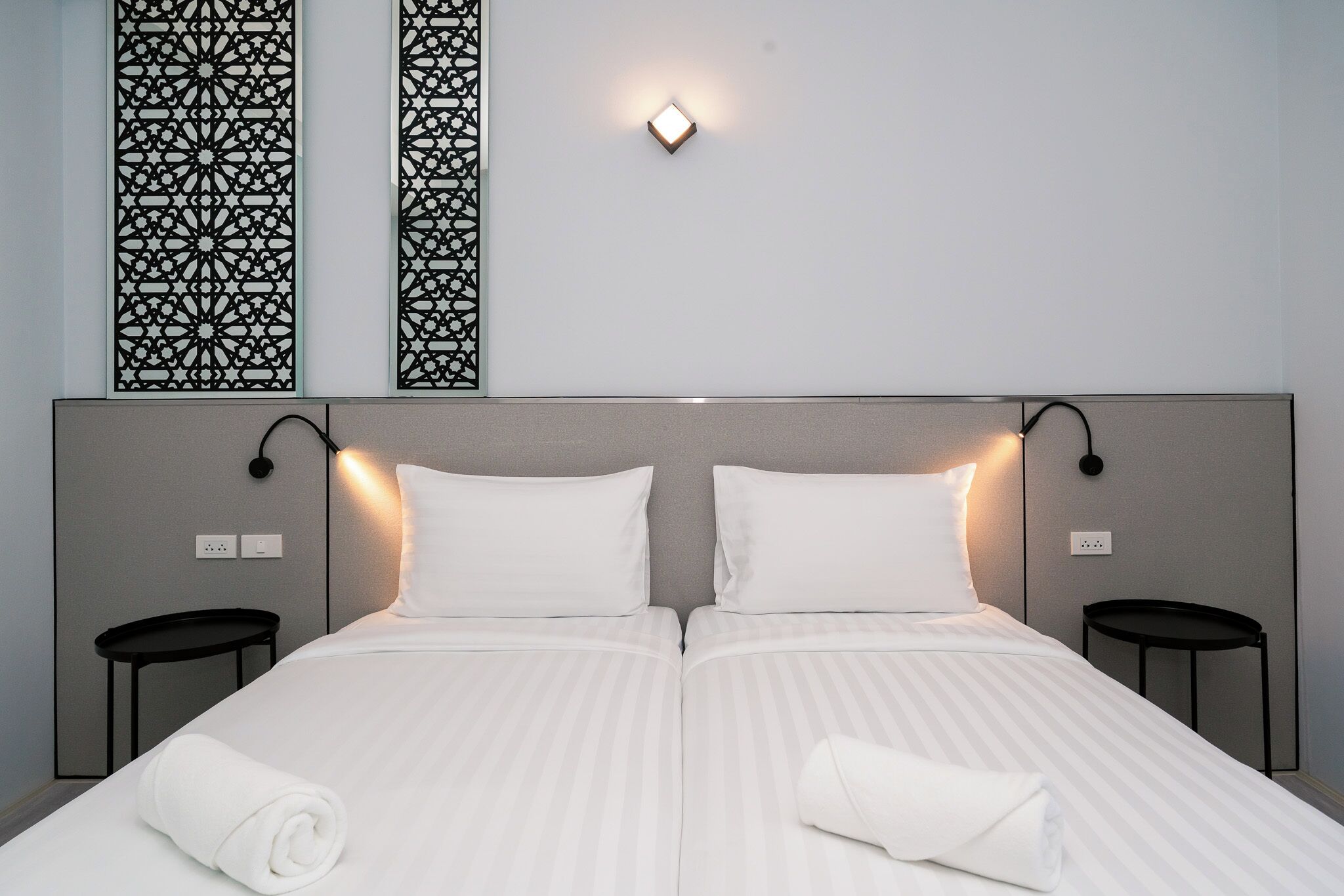 A double bed with white linens, two bedside tables, a wall-mounted light, and decorative panels.
