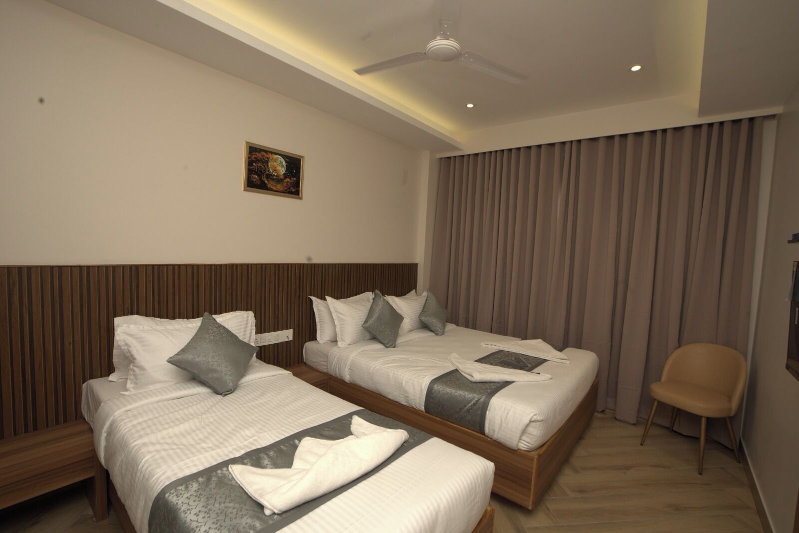 A hotel room with two beds, a ceiling fan, a painting on the wall, and a chair.