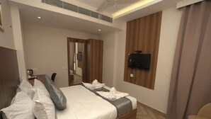A hotel room with a bed, a TV mounted on the wall, and a wooden floor. - Grand Sea Way (Chennai)