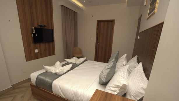 A modern hotel room with a neatly made bed, a flat-screen TV mounted on the wall, a wooden desk, and a chair. - Grand Sea Way (Chennai)