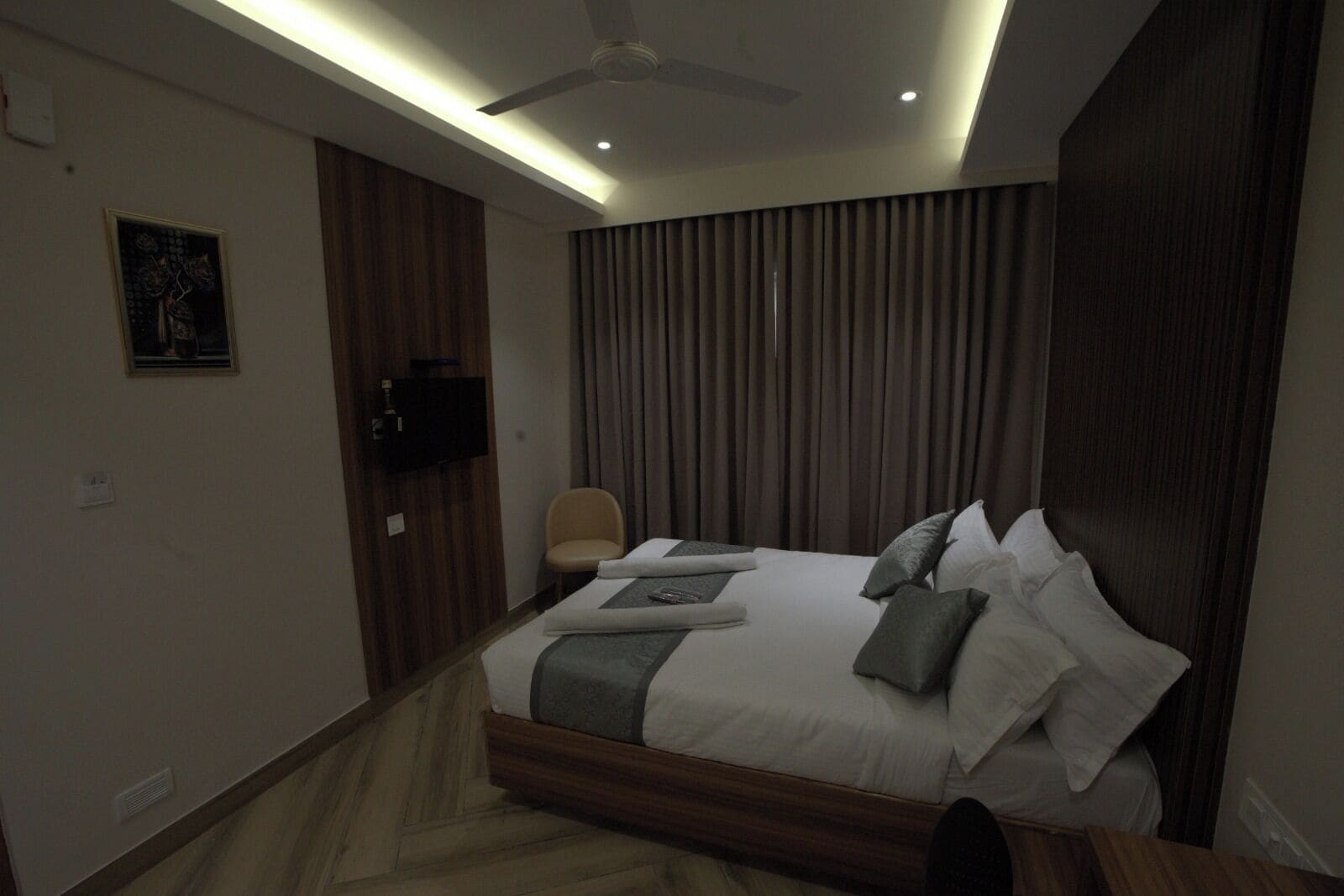 Una habitación de hotel moderna con una cama grande, un ventilador de techo y un televisor de pantalla plana montado en la pared.