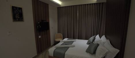 Una habitación de hotel moderna con una cama grande, un ventilador de techo y un televisor de pantalla plana montado en la pared.