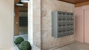 Un corridoio con pareti in marmo, una cassetta per posta grigia e due fioriere sferiche.