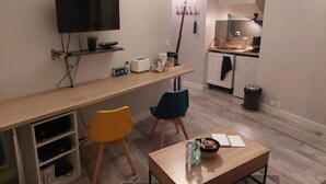 Un soggiorno moderno con televisione, una zona pranzo con sedie, un tavolino da caffè e un angolo cucina con lavello e mobili.