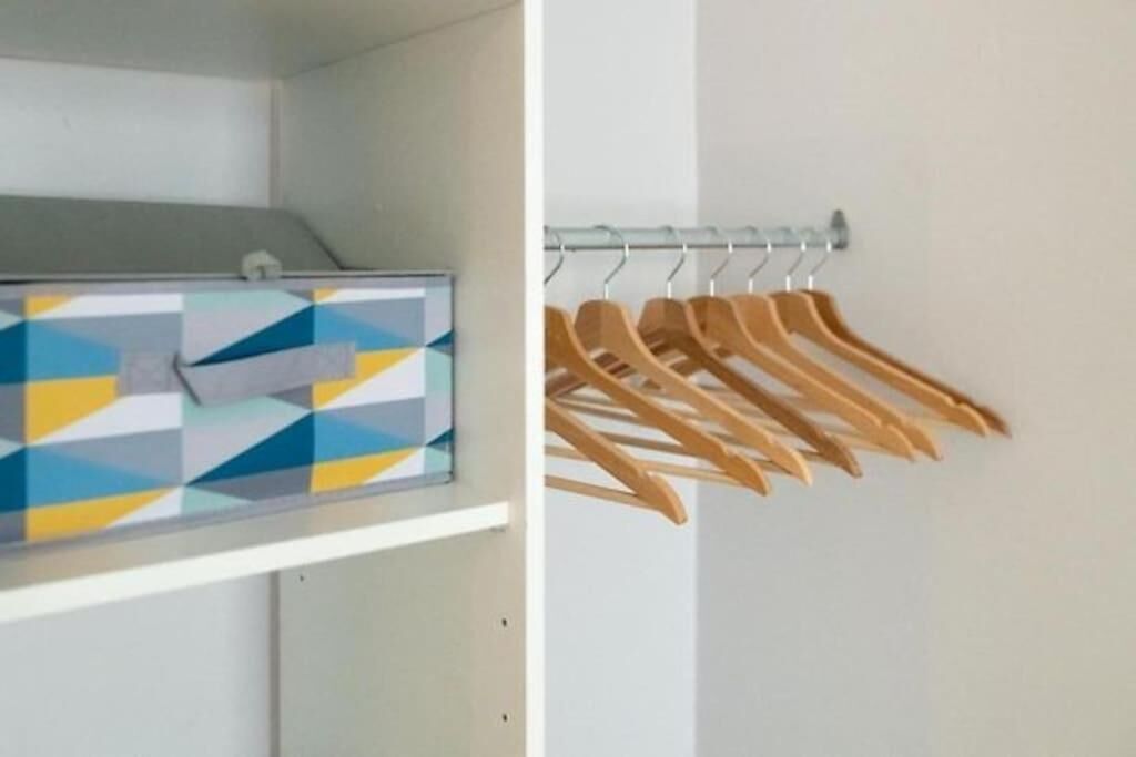 Ein Schrank mit einer Aufbewahrungsbox mit geometrischem Muster und Holzaufhängern an einer Kleiderstange.