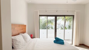 A hotel room with a large bed, a wooden headboard, a red bedside lamp, and a view of a balcony with palm trees. - La Residence with LOV (Cap Malheureux)