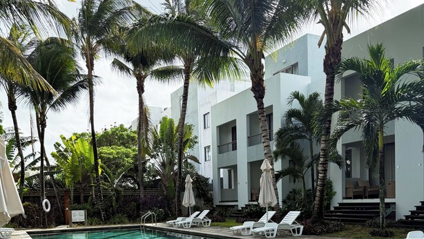 A swimming pool with clear water, surrounded by palm trees and lounge chairs. - La Residence with LOV (Cap Malheureux)