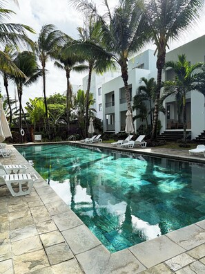 A swimming pool with clear water, surrounded by palm trees and lounge chairs. - La Residence with LOV (Cap Malheureux)