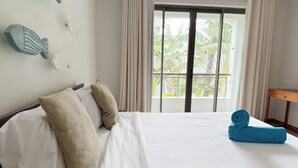 A hotel room with a large bed, two pillows, a rolled towel, a wooden nightstand, and a window with curtains. - La Residence with LOV (Cap Malheureux)