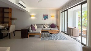A modern living room with a sofa, coffee table, and dining area. There is a ceiling fan, wall-mounted air conditioning, and a large sliding glass door leading to a balcony. - La Residence with LOV (Cap Malheureux)