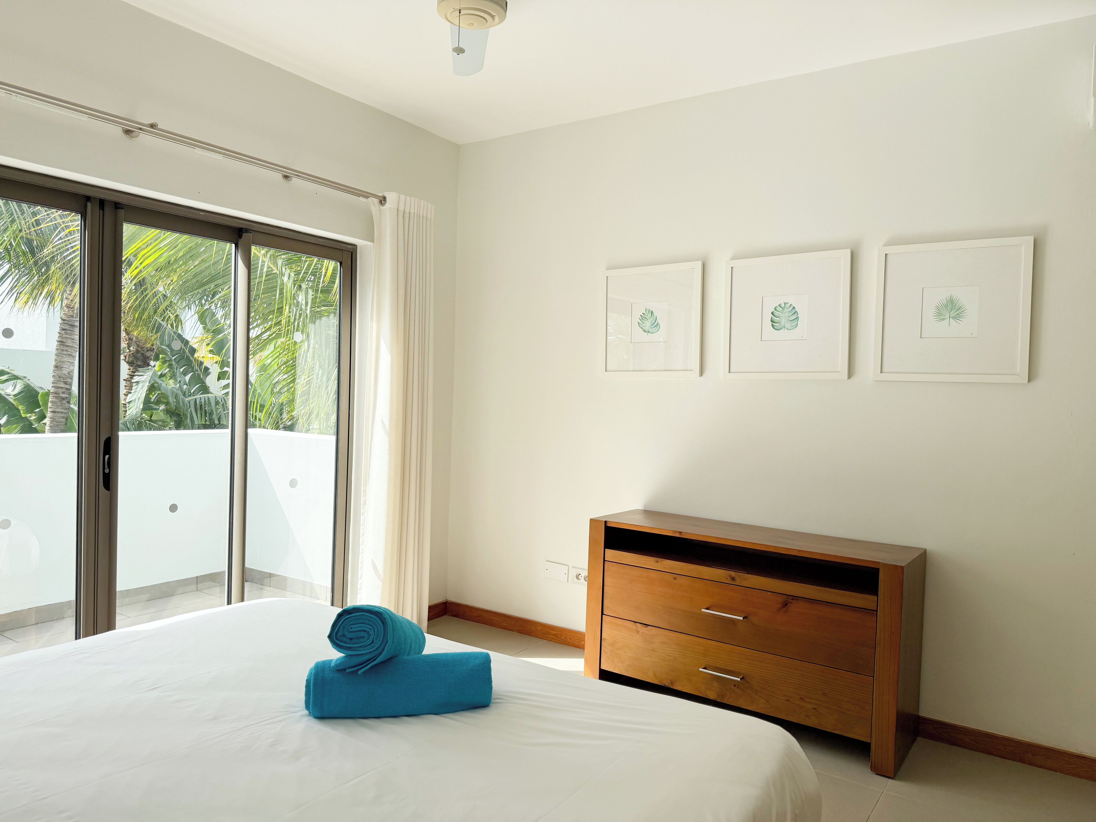 Una habitación de hotel con una cama, un aparador de madera y un balcón con vistas a palmeras.