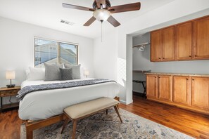Un dormitorio con cama, mesitas de noche, un banco, ventilador de techo y armarios de madera.