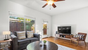 Ein Wohnzimmer mit Sofa, Sessel, Couchtisch, Fernseher und Deckenventilator.