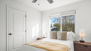 Ein Schlafzimmer mit einem Bett, Nachttischen, einem Fenster mit Jalousien und einer Tür.