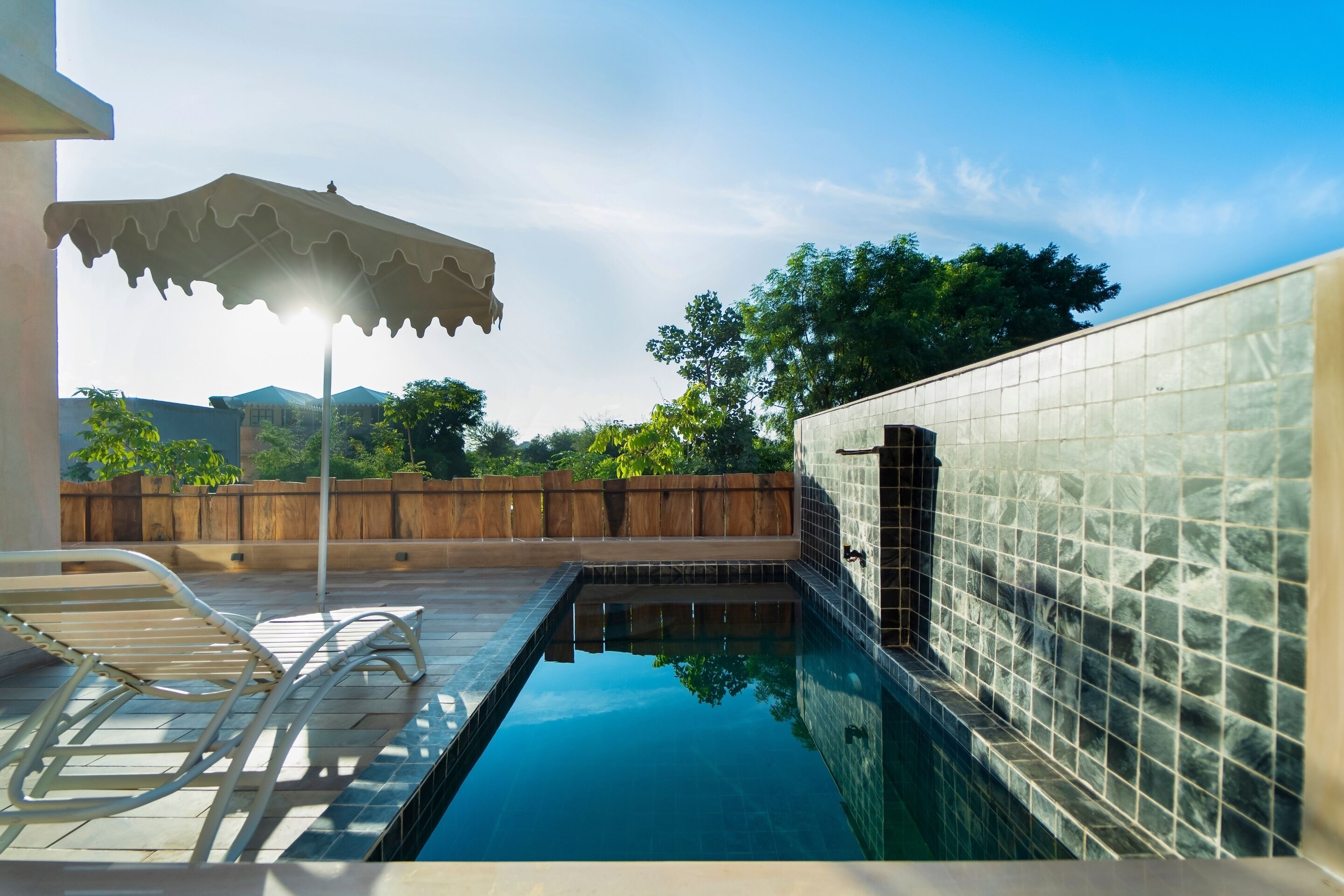 A swimming pool with tiled walls and a wooden deck with lounge chairs.