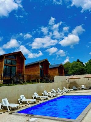 A wooden cabin with a swimming pool, surrounded by lounge chairs.