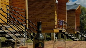 Ein Holztisch mit zwei Weingläsern und einer Weinflasche vor einem Holzhaus mit Treppe.