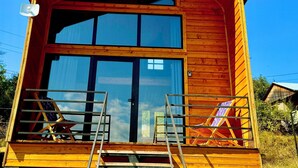 Eine Holzhütte mit großer Glassfront, rotem Dach und einer kleinen Veranda mit einer Leiter.