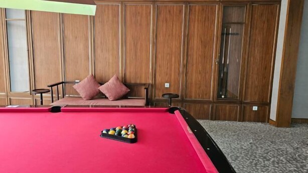 A pool table with balls in a room with wooden paneling and a sofa with cushions. - Premium Taman Anggrek Residences (West Jakarta)