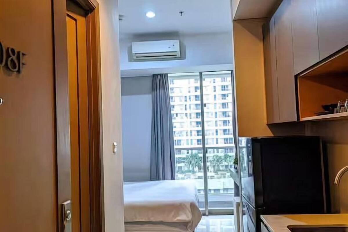 A hotel room with a bed, a kitchenette, and a large window with a view of a building.