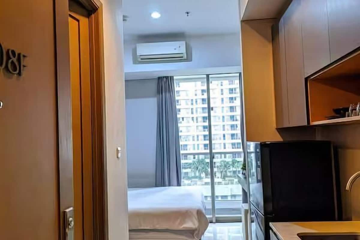 A hotel room with a bed, a kitchenette, and a large window with a view of a building.