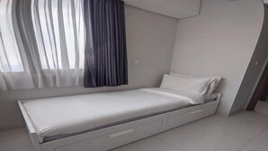 A modern bedroom with a single bed, a window with sheer curtains, and a white wall. - Premium Taman Anggrek Residences (West Jakarta)