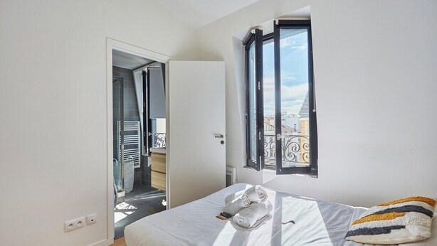 Ein Schlafzimmer mit Bett, Fenster, Tür und Blick ins Freie.