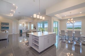 A modern kitchen with a central island, a dining area with a view, and a spacious living area with a large window. - Spacious Villa w Pool, Slides & Lush Nature Views (Kissimmee)