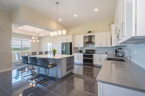 A modern kitchen with a central island, stainless steel appliances, and a large window providing natural light. - Spacious Villa w Pool, Slides & Lush Nature Views (Kissimmee)