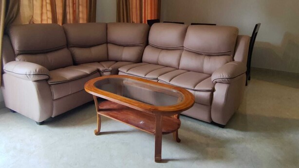 A sectional sofa with a wooden coffee table in a room with curtains. - 2D-Villastay (Kovalam)