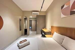Une chambre d’hôtel avec un lit, un bureau et une chaise. Un couloir mène à une autre pièce.