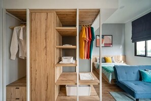 A modern bedroom with a built-in wardrobe, a bed with a blue headboard, and a window with a blackout blind. - Cove Prima (South Jakarta)
