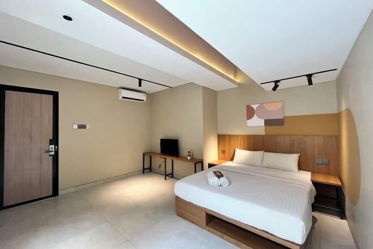 A modern hotel room with a bed, bedside tables, a TV, and an air conditioning unit.