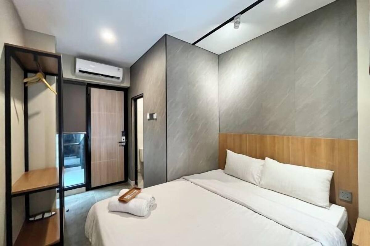 A modern hotel room with a large bed, a wardrobe, and an air conditioning unit.