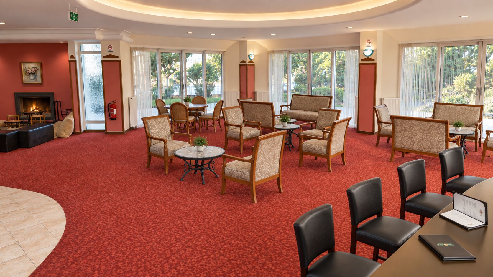 Un hall de hotel con alfombra roja, varias zonas de estar y grandes ventanales que dejan entrar luz natural.