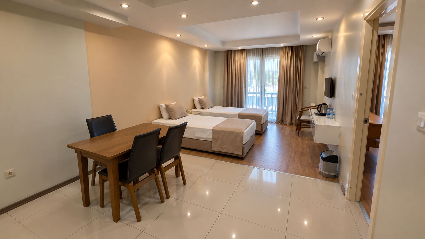 Una habitación de hotel con una mesa de comedor, dos camas, una kitchenette pequeña y un baño.